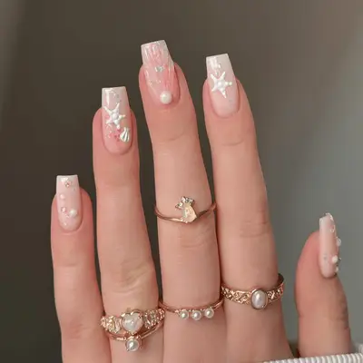Close up of nude square nails with glitter white seashell and starfish details.