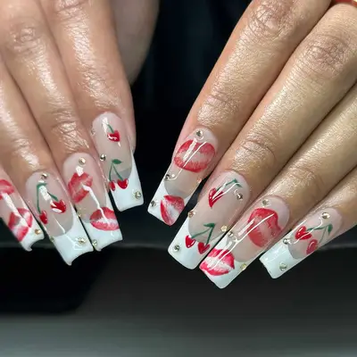 Hands with long nails decorated with designs showing cherries and lips, accented with small gemstones