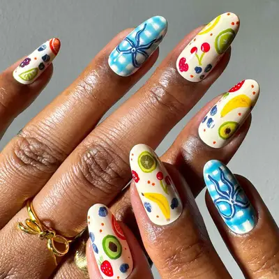 A hand showcasing nail art with colorful fruit and floral designs