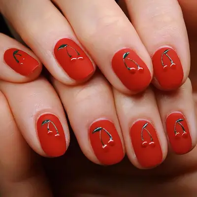 Hands with red nail polish and cherry designs on the nails