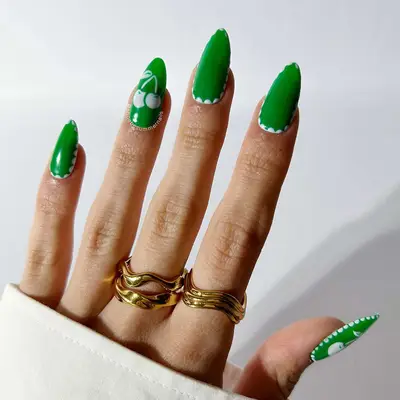 A hand with manicured nails featuring artistic green and white design, wearing gold rings