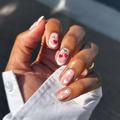 A hand with manicure featuring designs of cherries and hearts on the nails