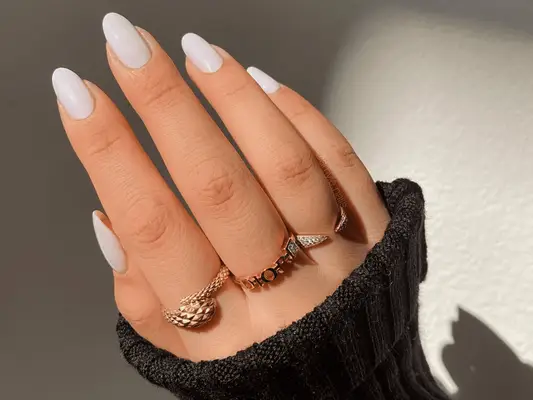 A hand with three rings and a manicure with cloudy white OPI Funny Bunny nail polish. 