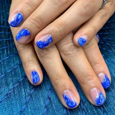 Manicure with blue and white marbled abstract wave designs on part of nails