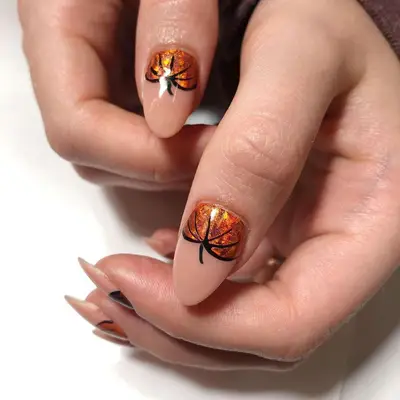 A manicure with a neutral base and pumpkin details at the cuticle