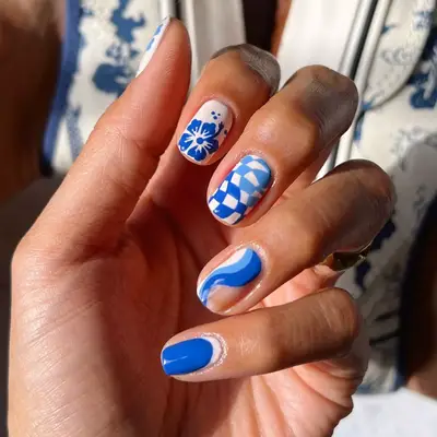 Close up of mix and match blue nails with waves, checkered print, and a hibiscus flower.