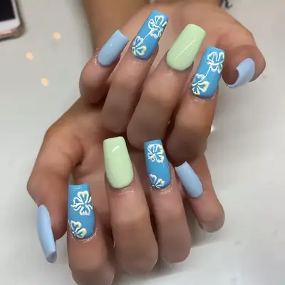 Close up of long nails is tonal shades of green and blue, with two hibiscus flor nail art accent nails.