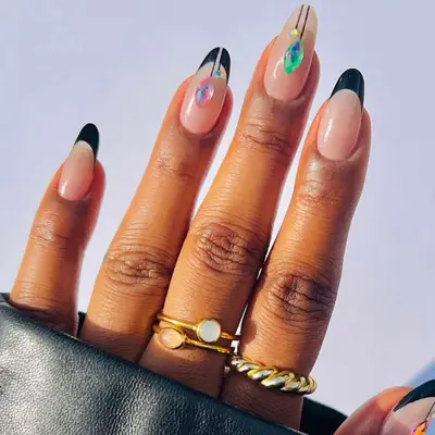 close up of hand showing off christmas manicure, with each nail having nude base, each nail different including black french tip and some nails with rhinestone drops in shape of ornaments