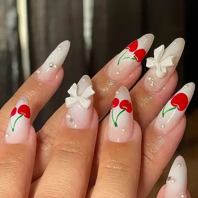 Milky white coquette nails with 3D bow accents, pearls, and cherry nail art