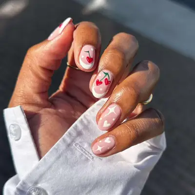 White doodle nails with French tips, star, heart, and polka dot accents with cherry nail art