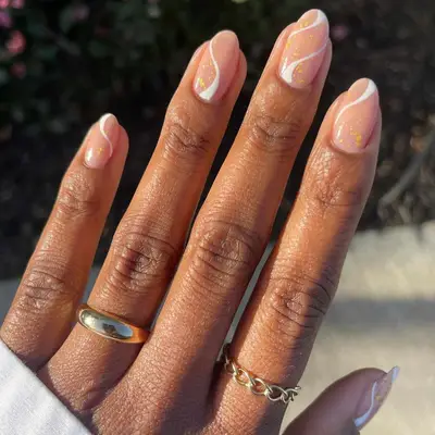 White wavy nails with gold flecks on a nude base