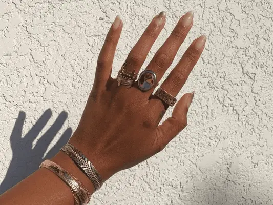 A hand in the sunlight showing a nude with gold foil manicure.