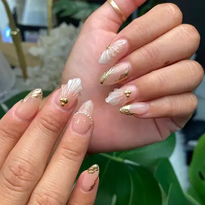 Almond-shaped nails with gold asymmetrical cutout tips with gel seashell designs and gold embellishments