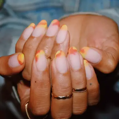 Yellow, red, and orange powdered tips on a manicure.
