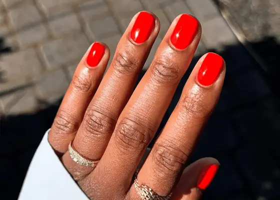 A hand with neatly polished red nails wearing delicate rings