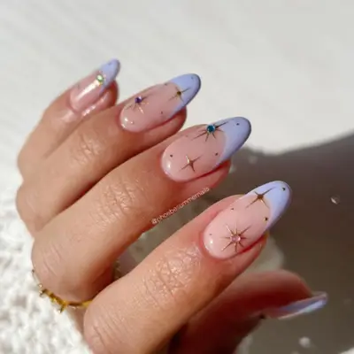 French manicure with periwinkle tips, gold star designs, and colorful gems