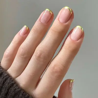 Close up of a French manicure with a clear base and gold tips