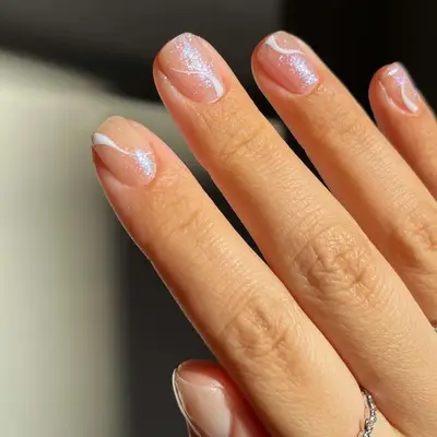 Close up of a short manicure with white squiggles and a glittery base polish