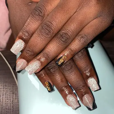 Black and gold glittery nail design with yellow gems on pinky finger