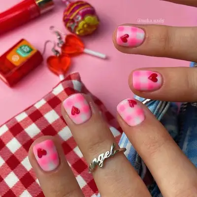 Close shot of hands with pink and heart-themed nail art on a background of various small items and accessories