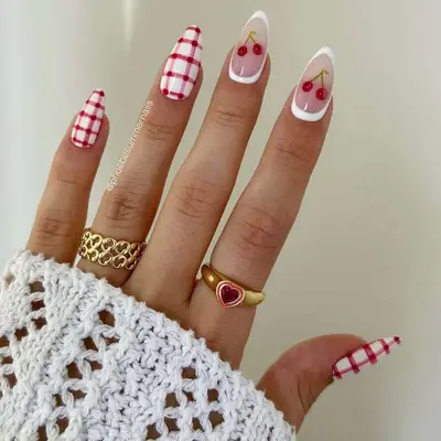 A hand with manicured nails featuring red checkered and cherry-themed designs