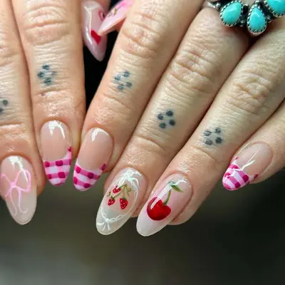Close-up of hands with nail art featuring cherries, gingham patterns, and rings adorned with turquoise stones