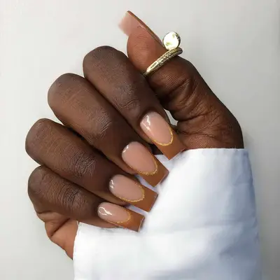 Close up of a brown-tipped French manicure with gold outline details