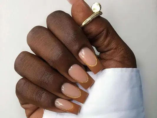 A French manicure with brown-caramel tips and a gold line accent