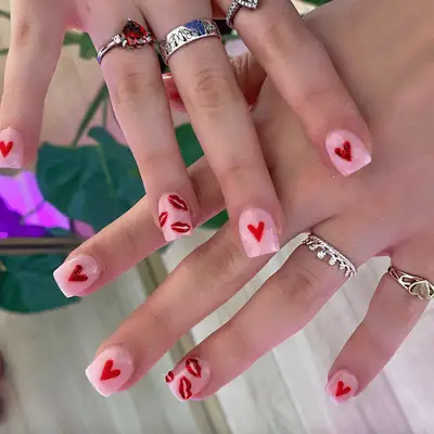 Pink, square-shaped acrylic nails with red hearts and smooched-lips nail design