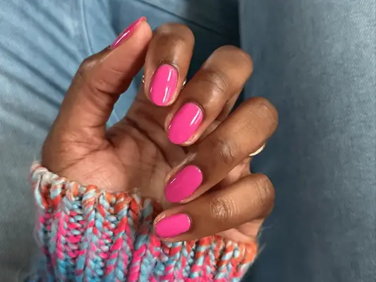 A hand with hot pink short nails and the sleeve of a rainbow sweater