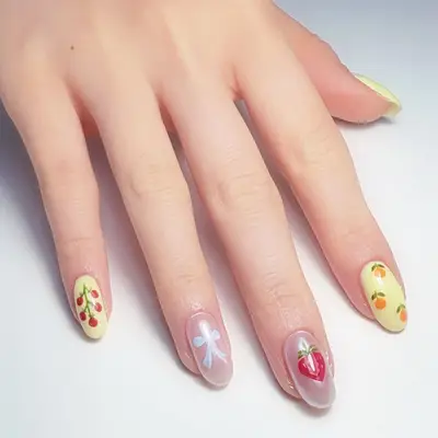 Hand with decorative nail art featuring fruit and bow designs