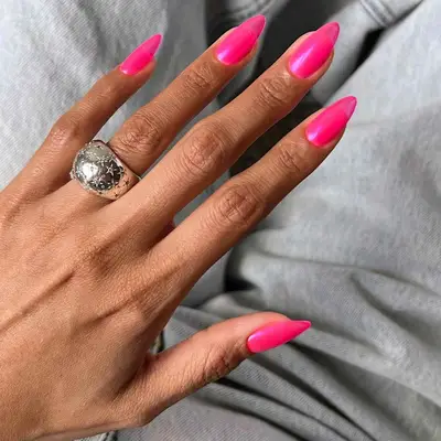 A hand with a ring, nails with long pink polish
