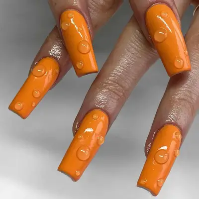 Close-up of hands with orange nails featuring a glossy finish and decorative water drop details