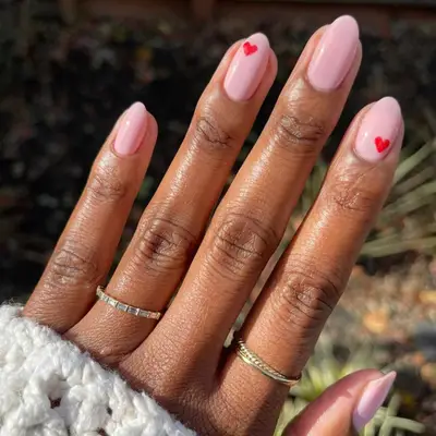 Bubble bath pink nails with two small red hearts on the pointer and ring fingers.