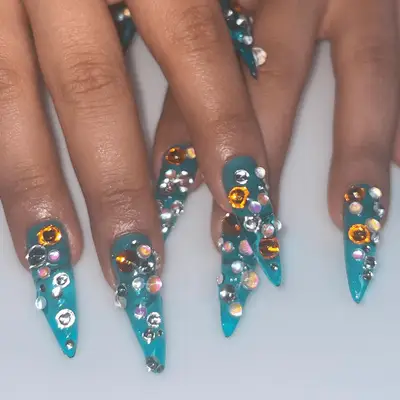 Close up of long blue nails with multicolor rhinestone crystals on each nail. 