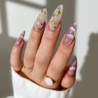 Hand with celestial-themed nail art, featuring moons, stars, and clouds on long almond-shaped nails