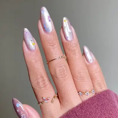 Hand with long almond-shaped nails decorated with floral designs, wearing gold and gemstone rings
