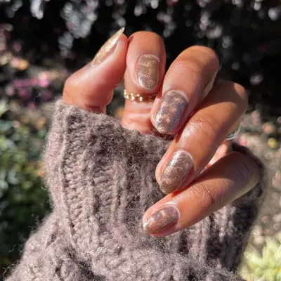 A close-up of a hand with manicured nails featuring a shiny bronze crushed velvet design
