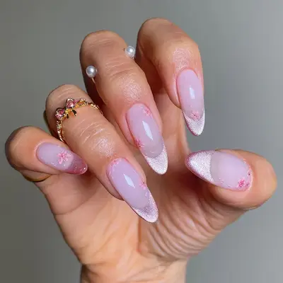 Close-up of a hand with manicured nails featuring a pink and white velvety cherry blossom design, accessorized with rings