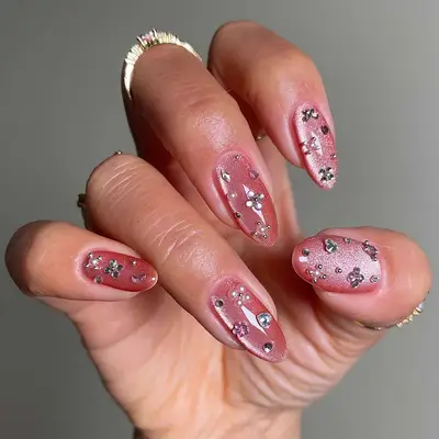 Manicured hand showing bedazzled nail designs with a blush velvet style