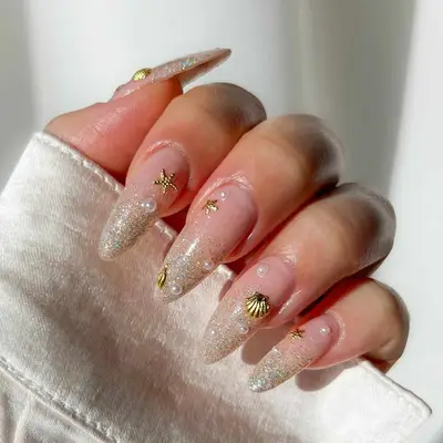 Manicure featuring long nails with a seashell and nautical design on a glittery background