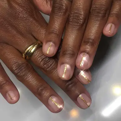 Close-up of manicure with neutral base and gold glitter central stripes