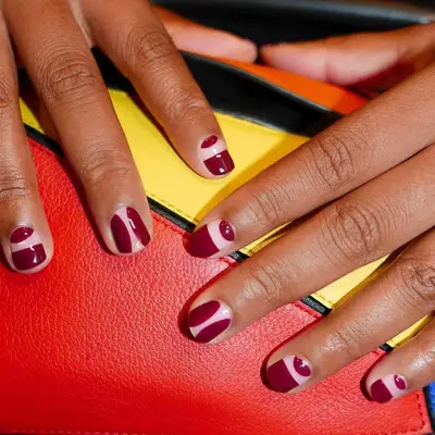 Close-up of manicure with minimal neutral base and abstract cranberry red nail designs