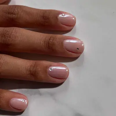 Close-up of short nails with pearlescent pink base and small gemstone accents