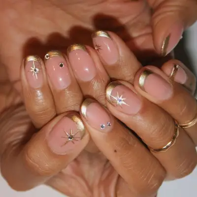 Manicure with gold French tips, star designs, and small gemstones
