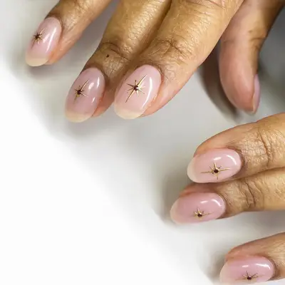 Manicure with pink-toned neutral base and gold star designs
