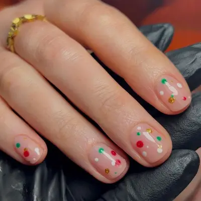 Short nails with neutral base and red, white, green, and gold glitter dot designs