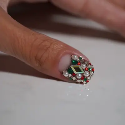 Close-up of short nail with pearls, red and green gems, and negative space cuticle half-moon