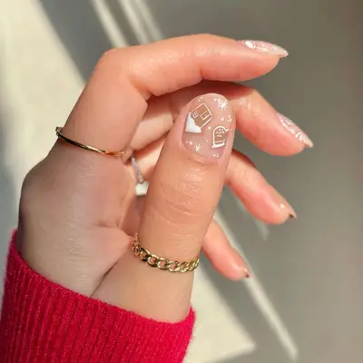 Close-up of manicure with neutral base and snowy house and mitten designs