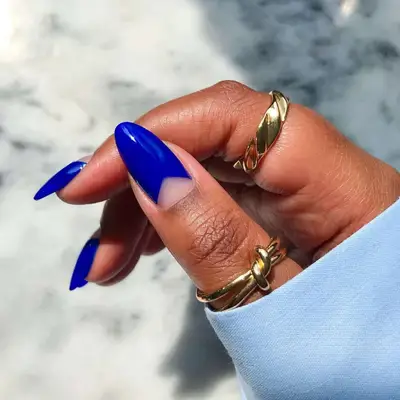 A hand with cobalt blue nail polish and gold rings